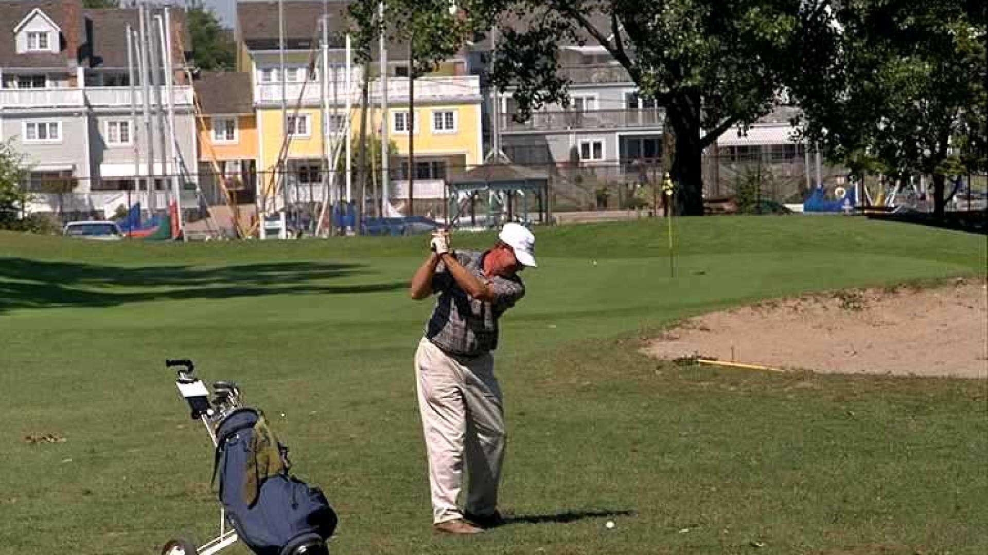 Person playing golf. There are buildings in the background.