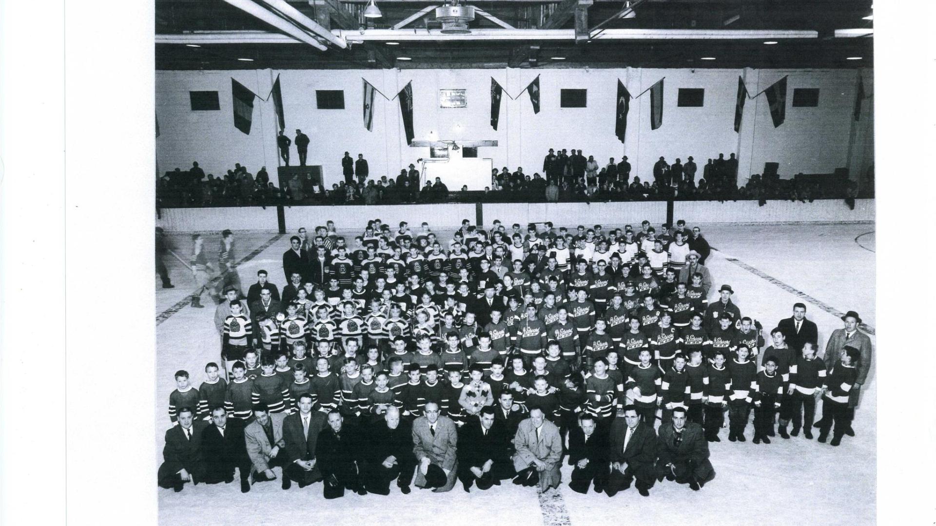 Group photo of hockey teams incide an ice rink. The photograph is black and white.