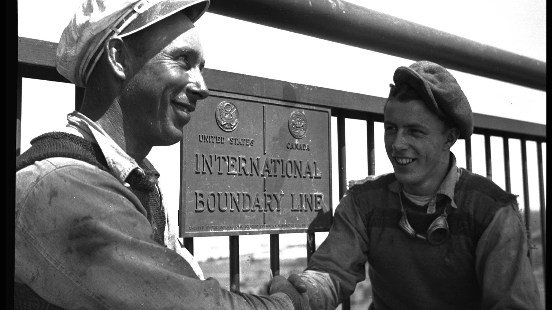 Two men shaking hands in front of a plaque.