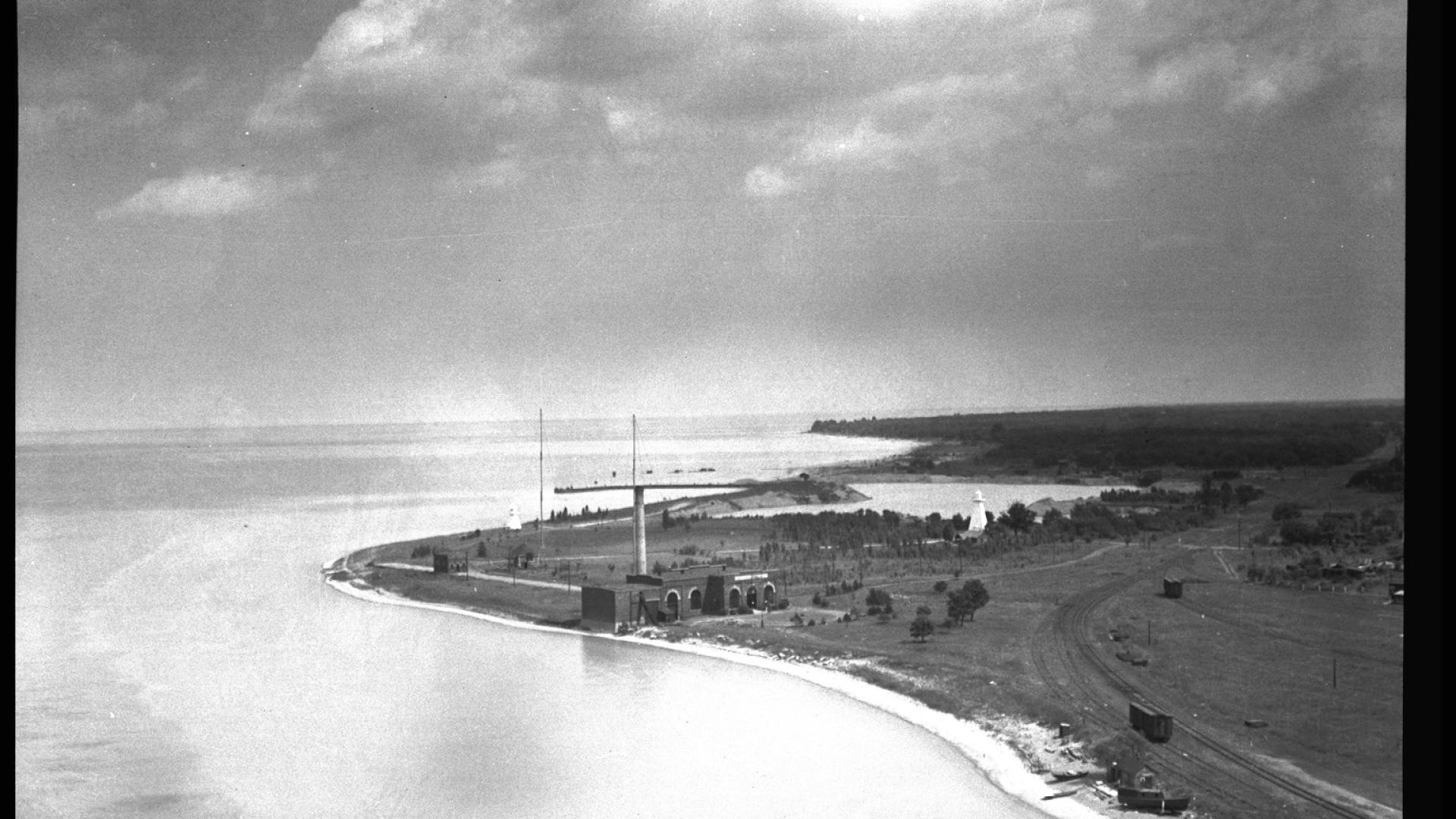 Aerial view of bridge construction. There is land to the right and water to the left. The bridge construction stands tall on the land side.