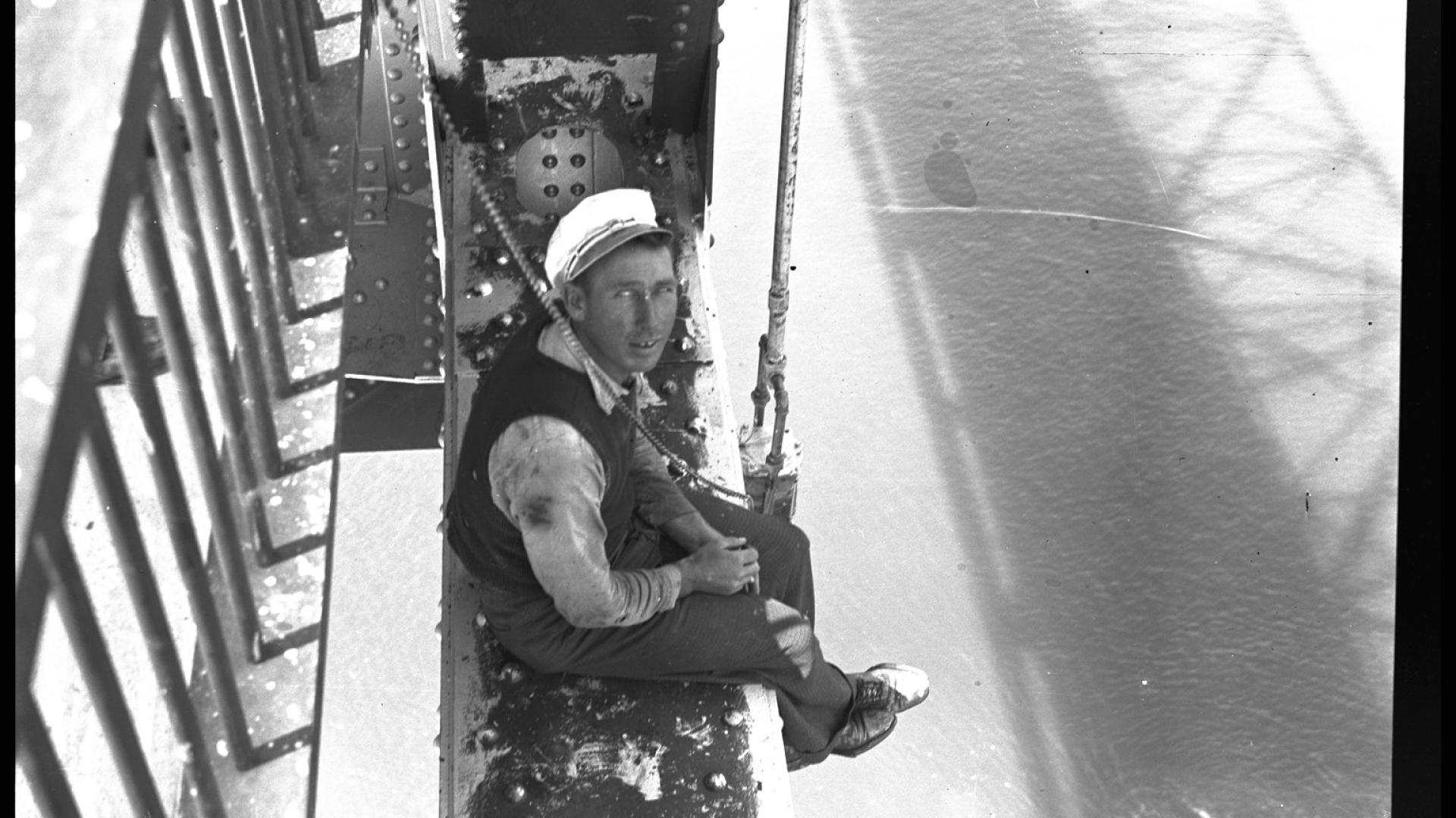 Two men sitting on edge of bridge construction. The men are smiling at the camera.