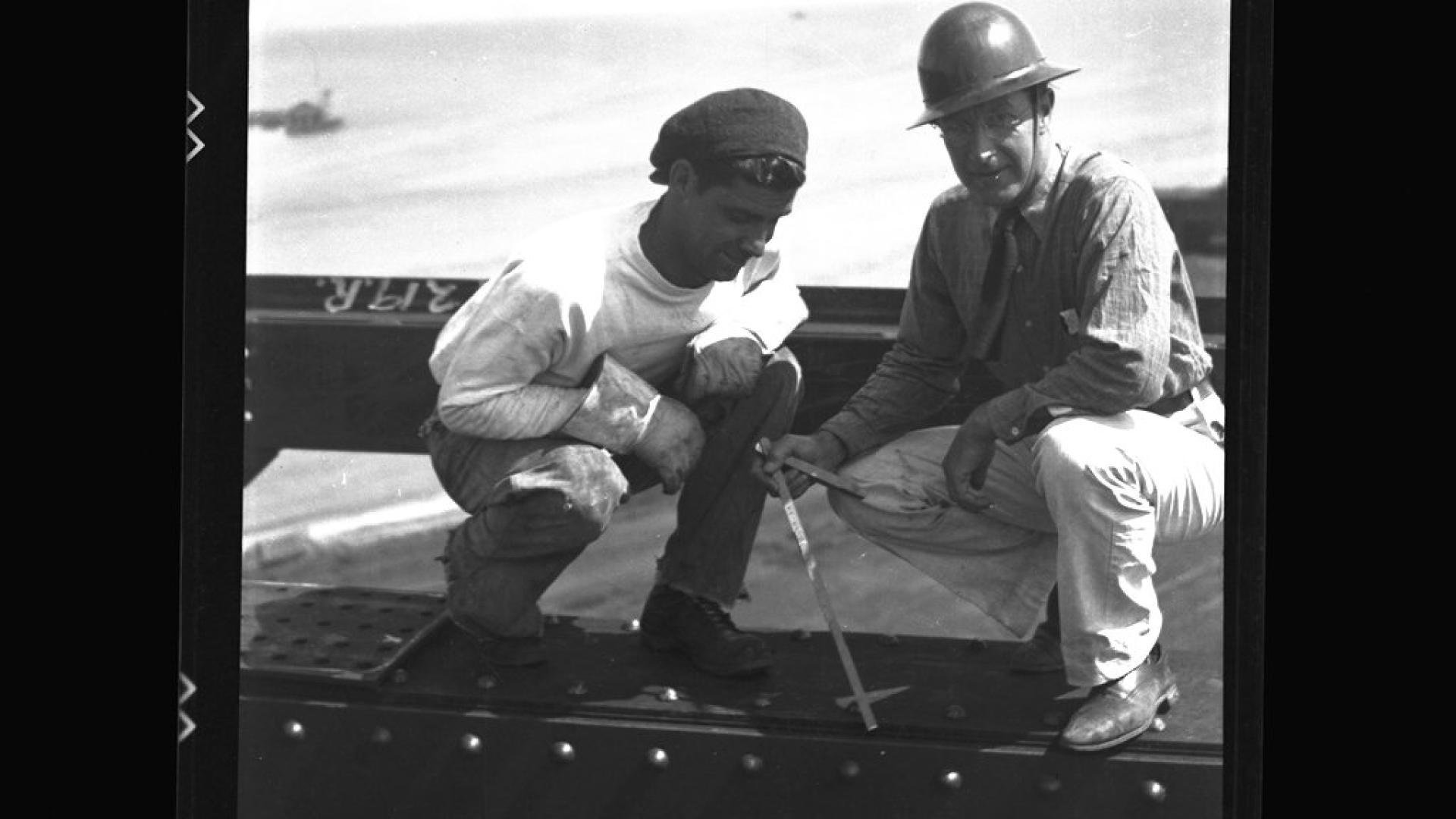 Two construction workers sitting and working on bridge. 