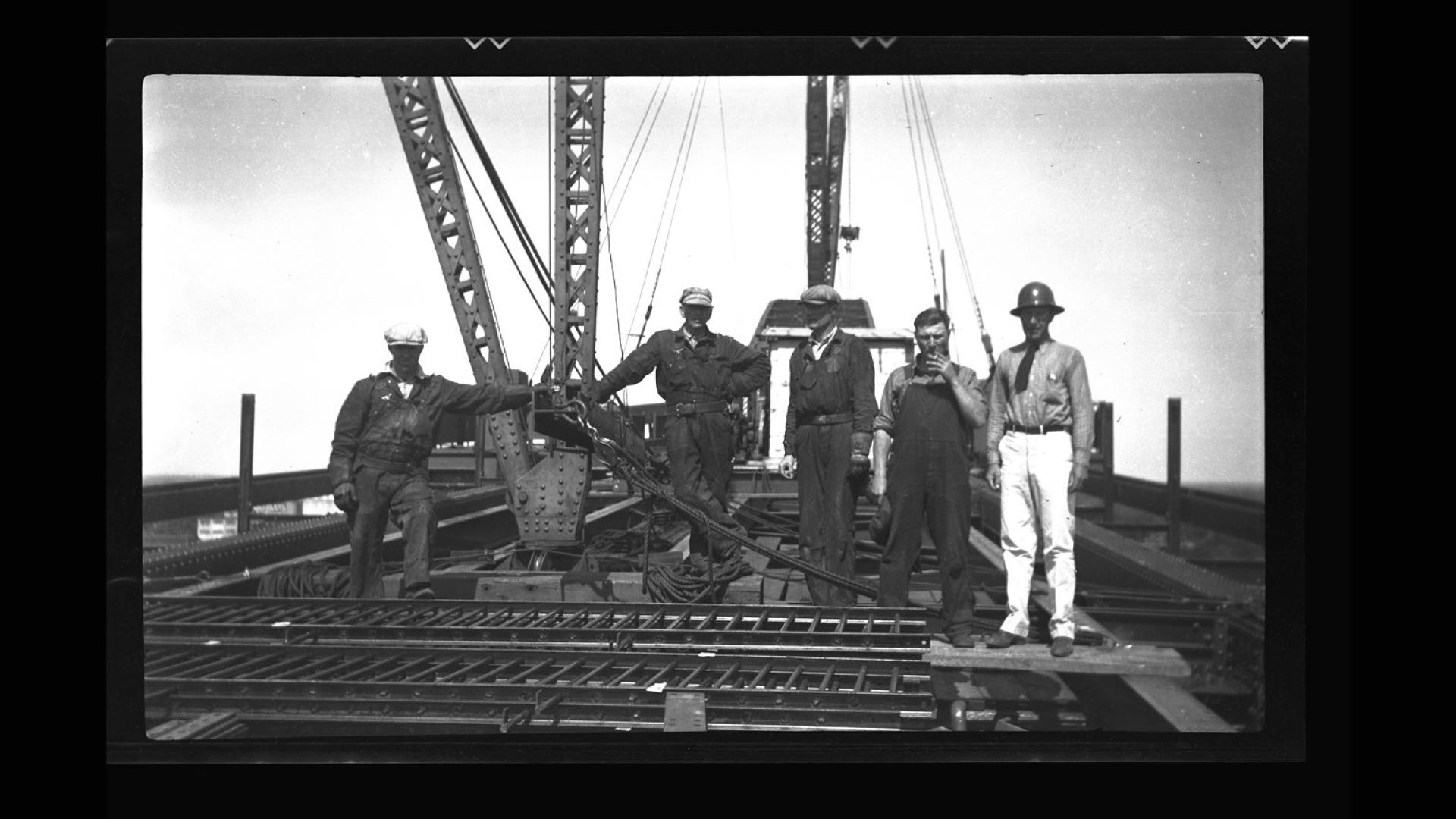 Construction crew on top of bridge being constructed. There is heavy construction machinery in the background