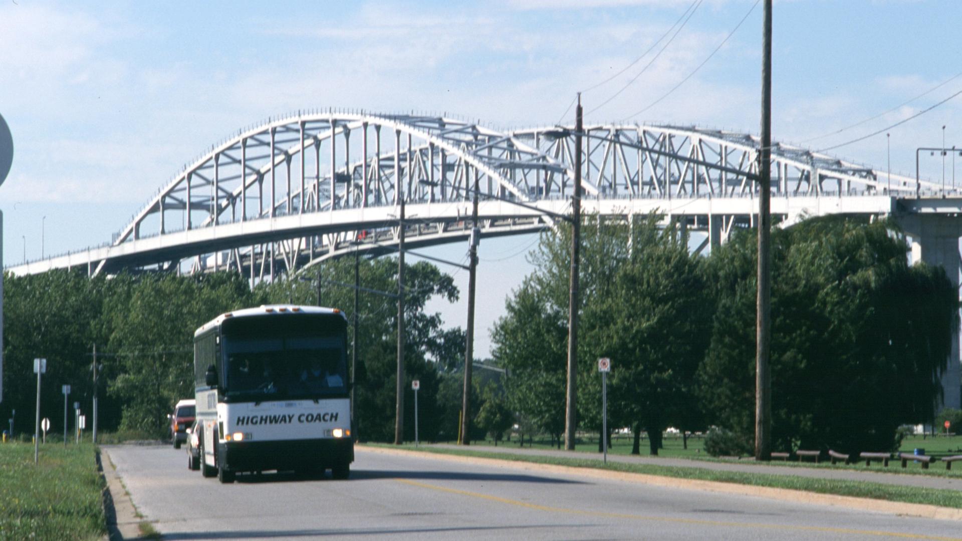 Coach bus driving on the foreground as the bridge stand tall in the background.