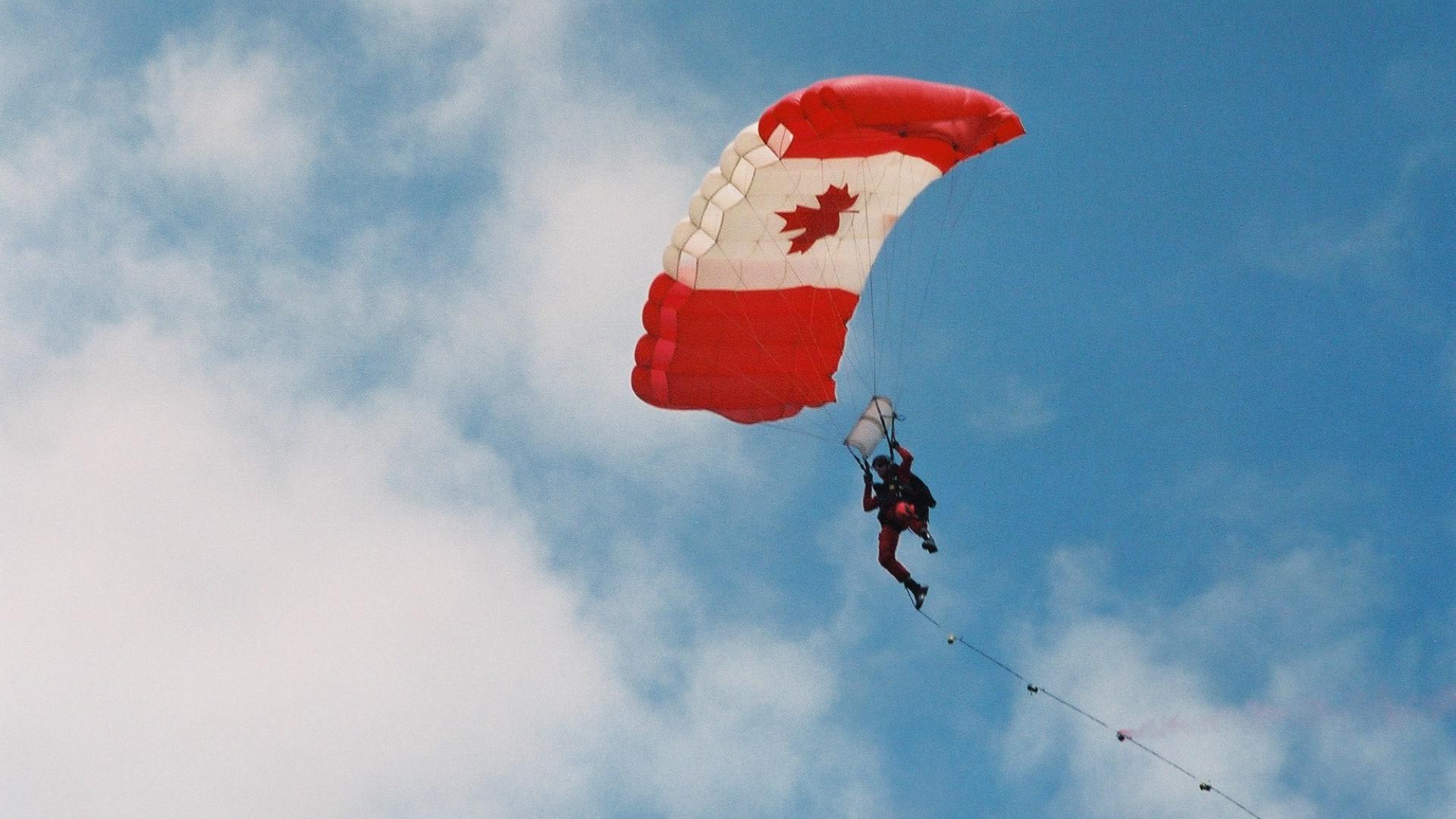 Parachuter sailing through the sky. The parachute has a Canadian flag design.