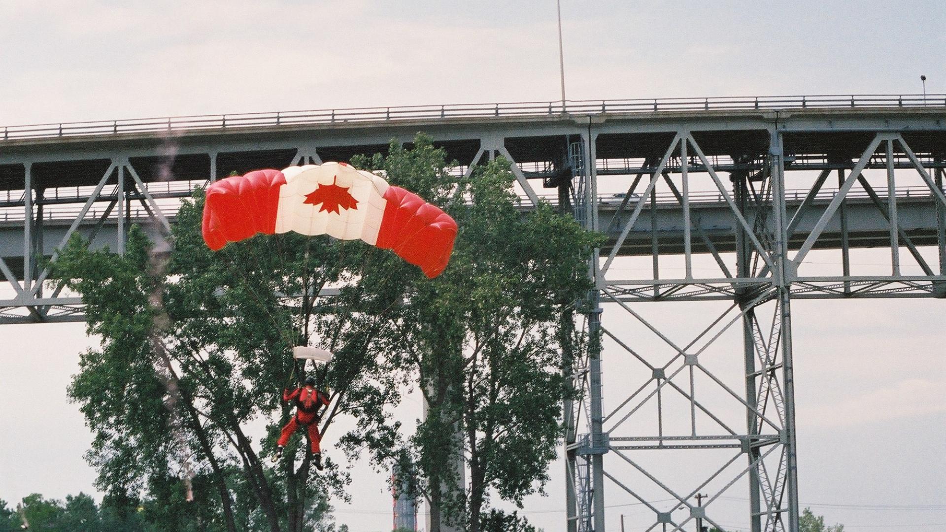 Parachuter landing on ground. The parachute has the Canadian flag design.