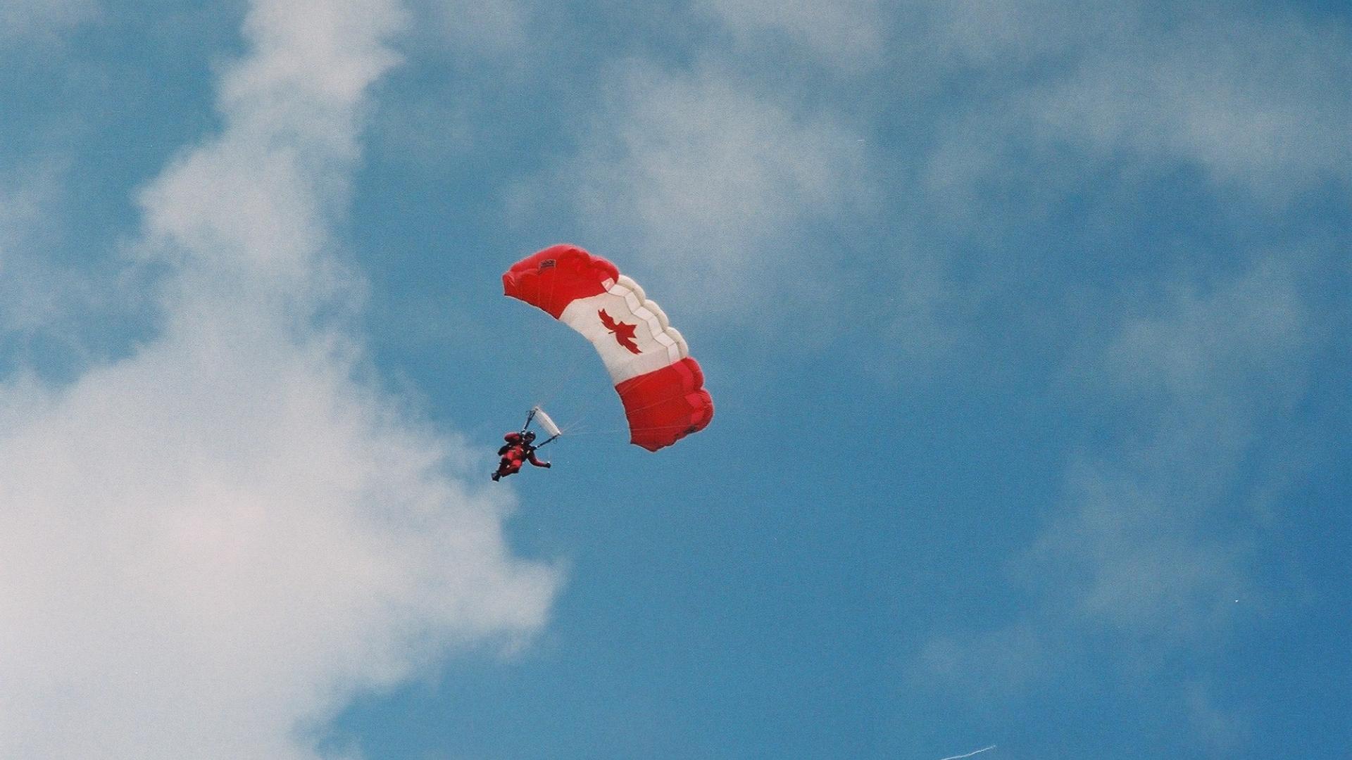 Parachuter sailing through the sky. The parachute has a Canadian flag design.