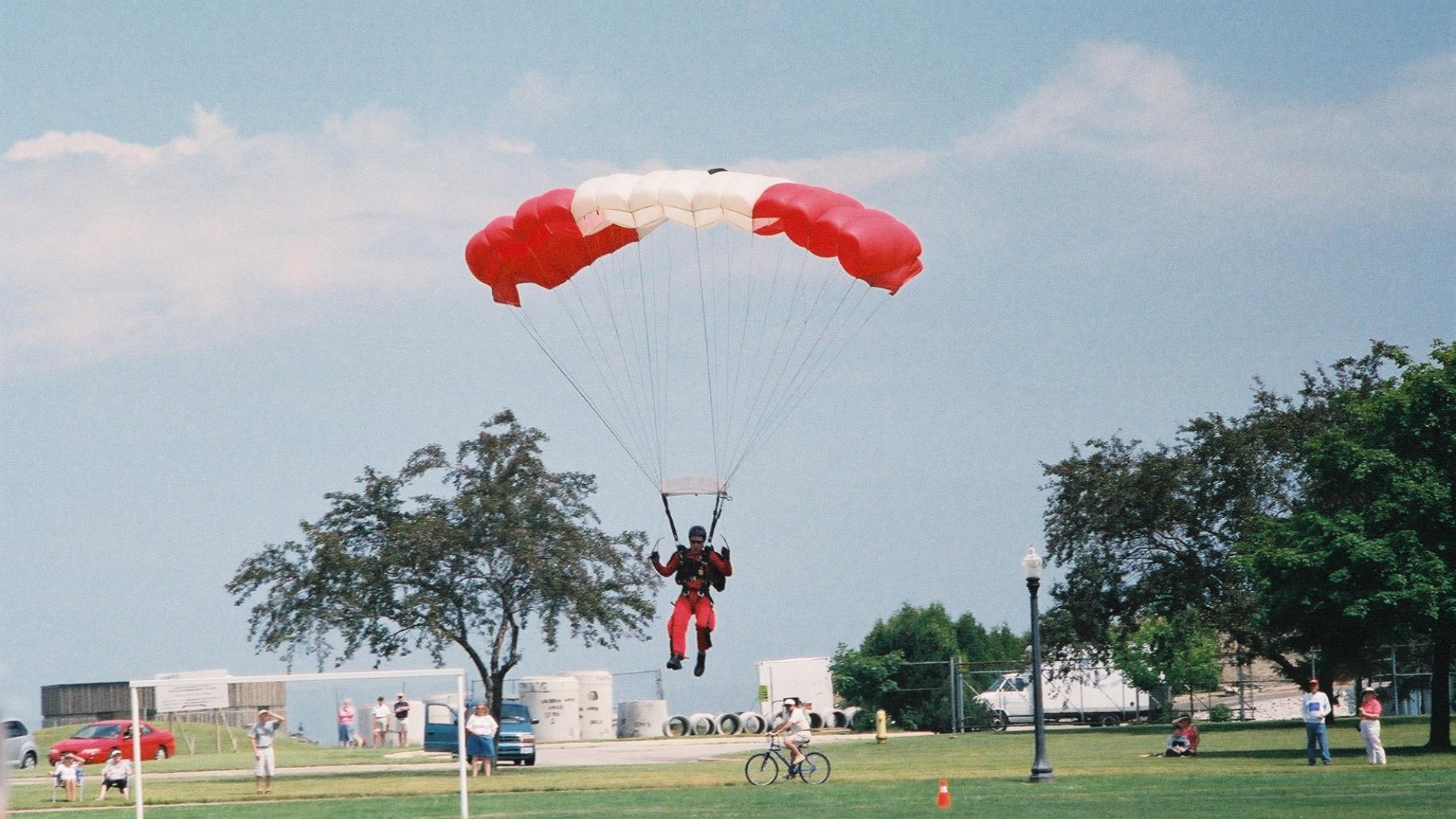 Parachuter landing on green patch of land. The parachute has a Canadian flag design.