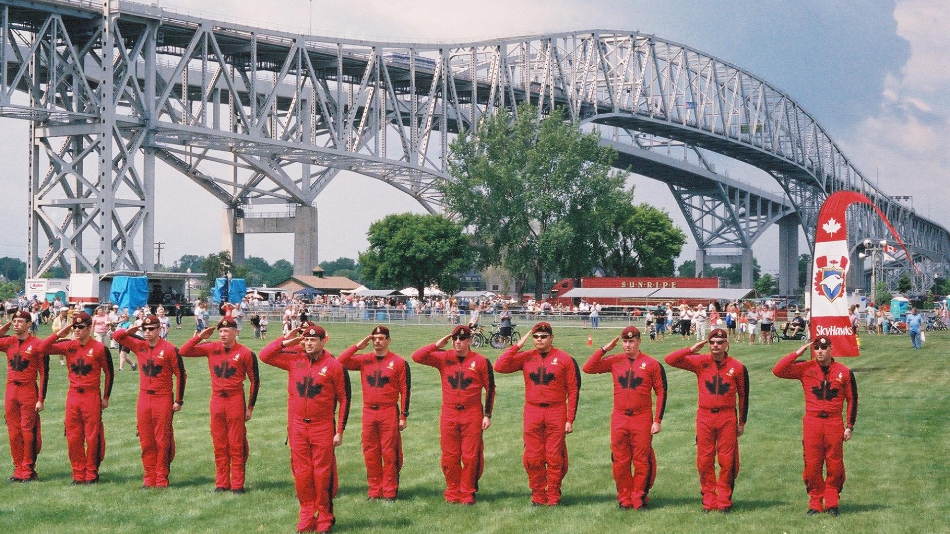 Group of men in red jumpsuits saluting facing forward. The bridge stands tall in the background.