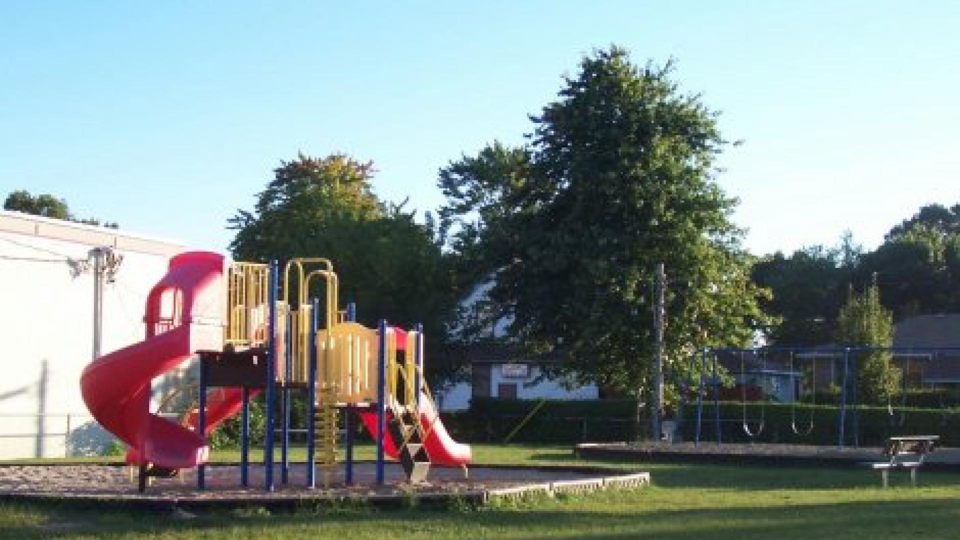 Playground with a jungle gym and a picnic table on the side. There are some green trees in the background.