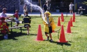 Person handling firehouse in yellow firesuit. There are bystanders spectating the person with the firehose. 